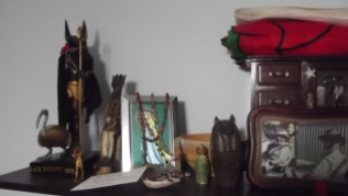 Left side of the ancestor shrine. Anubis, Djehuty, and Aset as Lady of the West sit at the end. Then there's my Marian shrine, along with two canopic jars and a libation bowl. The jewellery case and the folded up Welsh flag on top of it belonged to my maternal grandparents, who are in the photo in front of it.