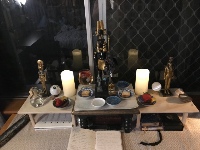 a photograph of an egyptian altar with a statue of Sobek at the centre, Sekhmet on the left, and Hetheru on the right, along with candles, some crystals, and offerings for the New Year. 